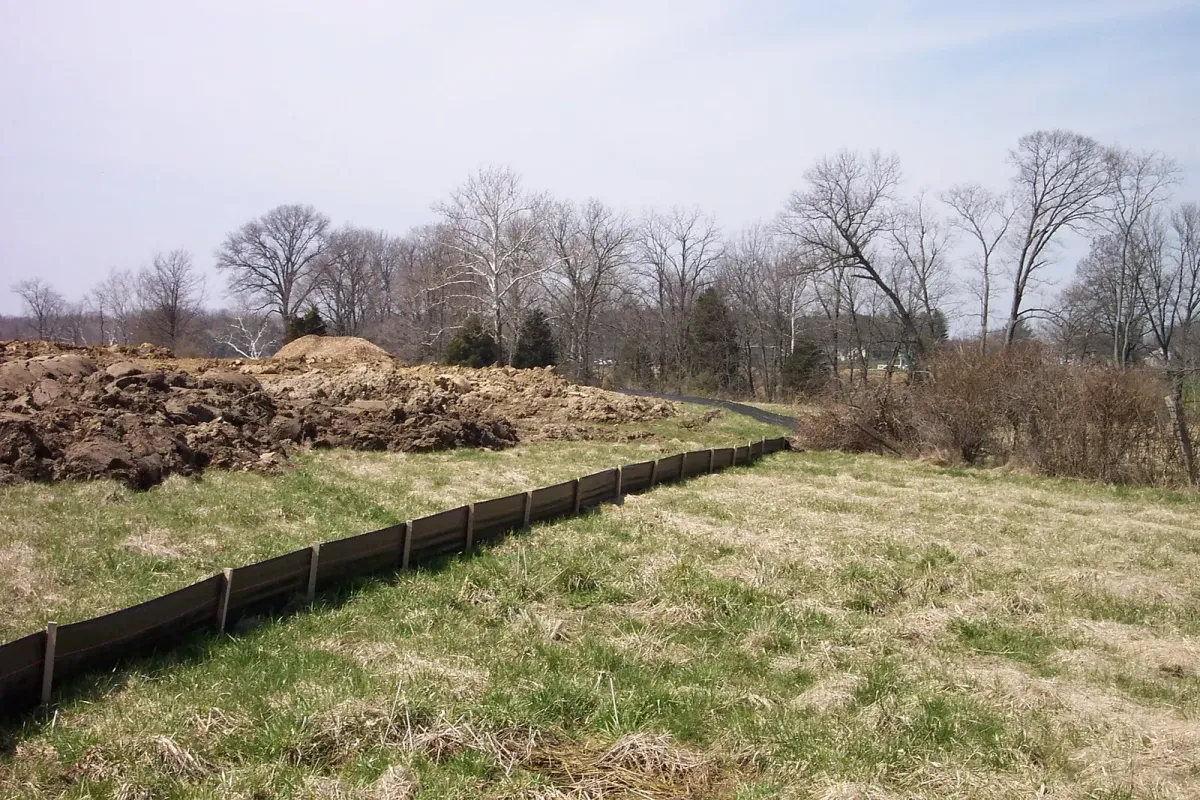 Silt fence beside piles of excavated soil on a construction site in open grassland
