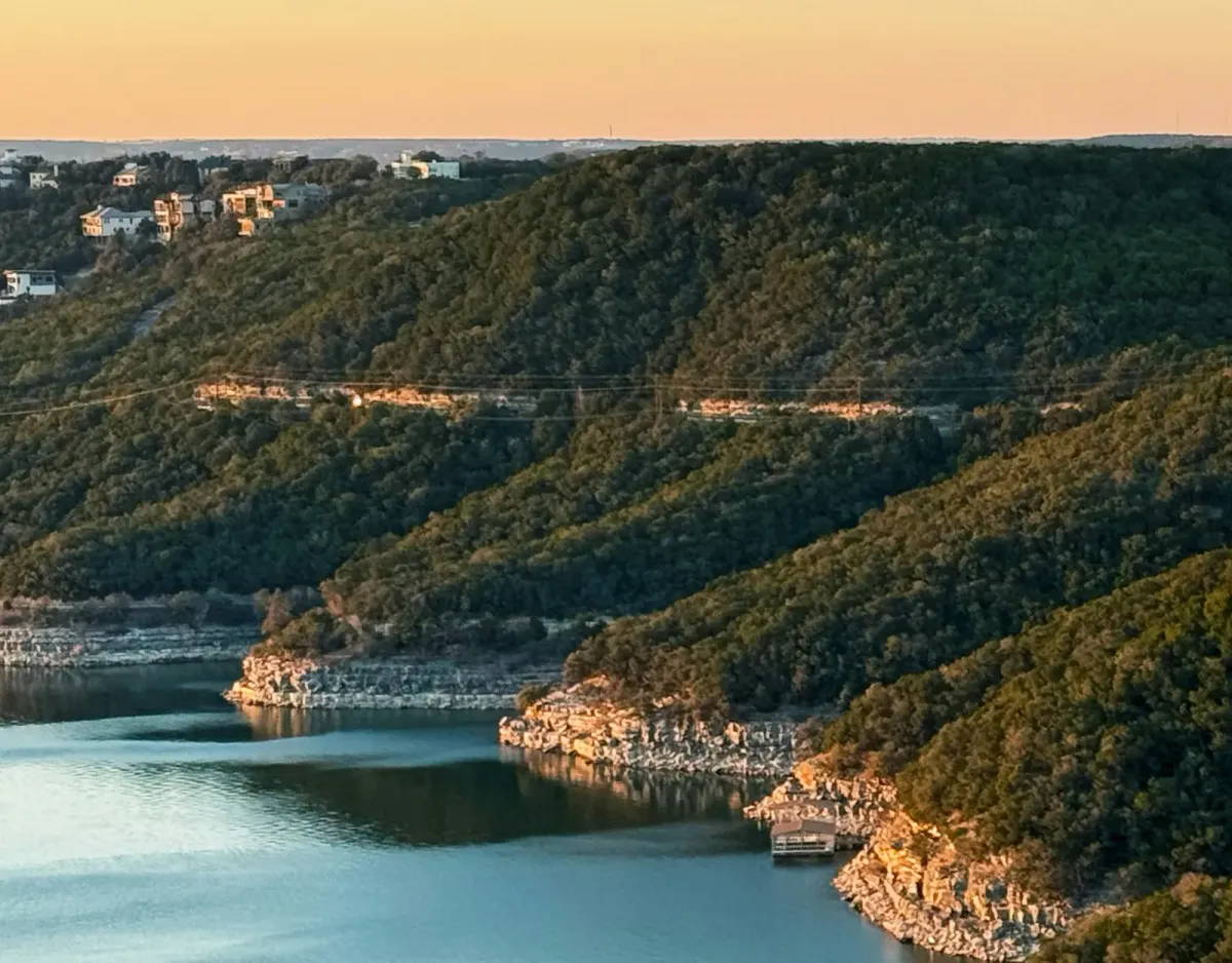 Wooded hills and limestone shoreline above Lake Travis in the Texas Hill Country at sunset