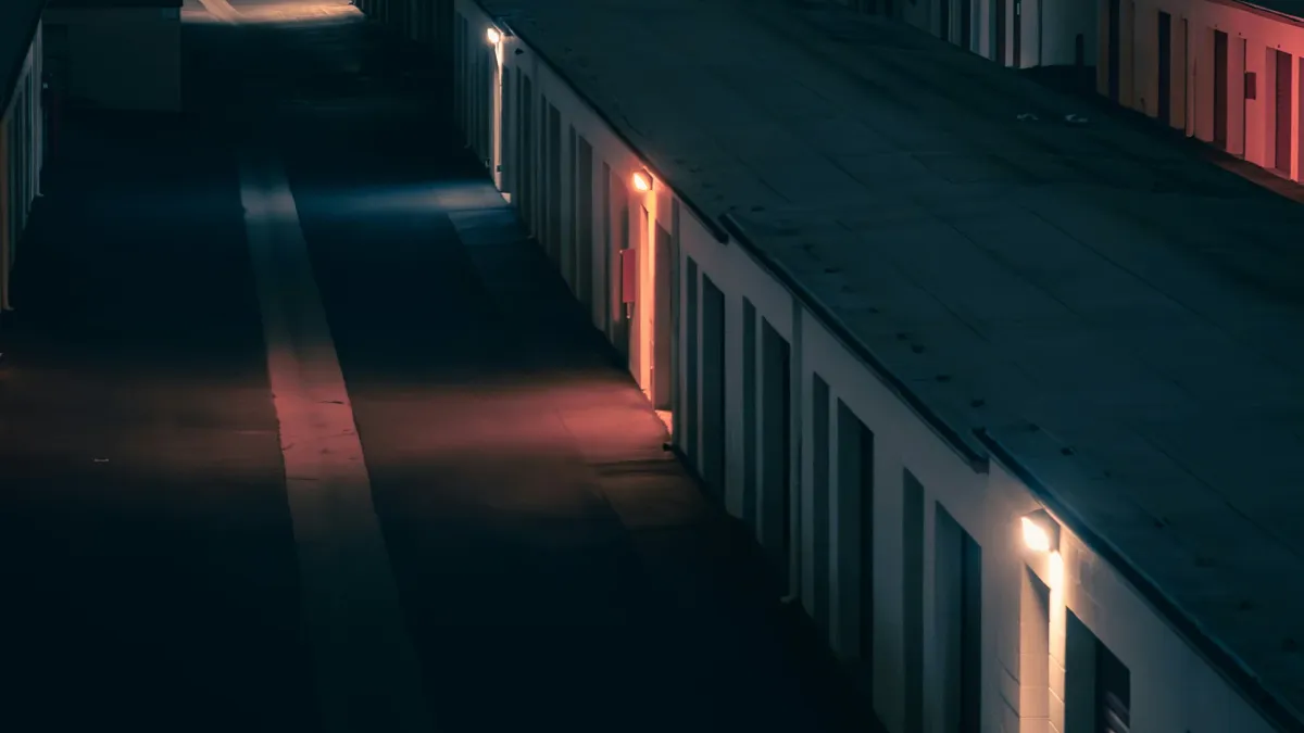 Rows of single-story storage units with roll-up doors along a lit drive aisle at night in a city